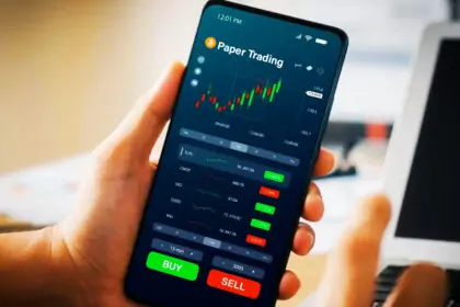 A person holding the mobile device with Bitcoin Paper Trading screeen in Dark theme.